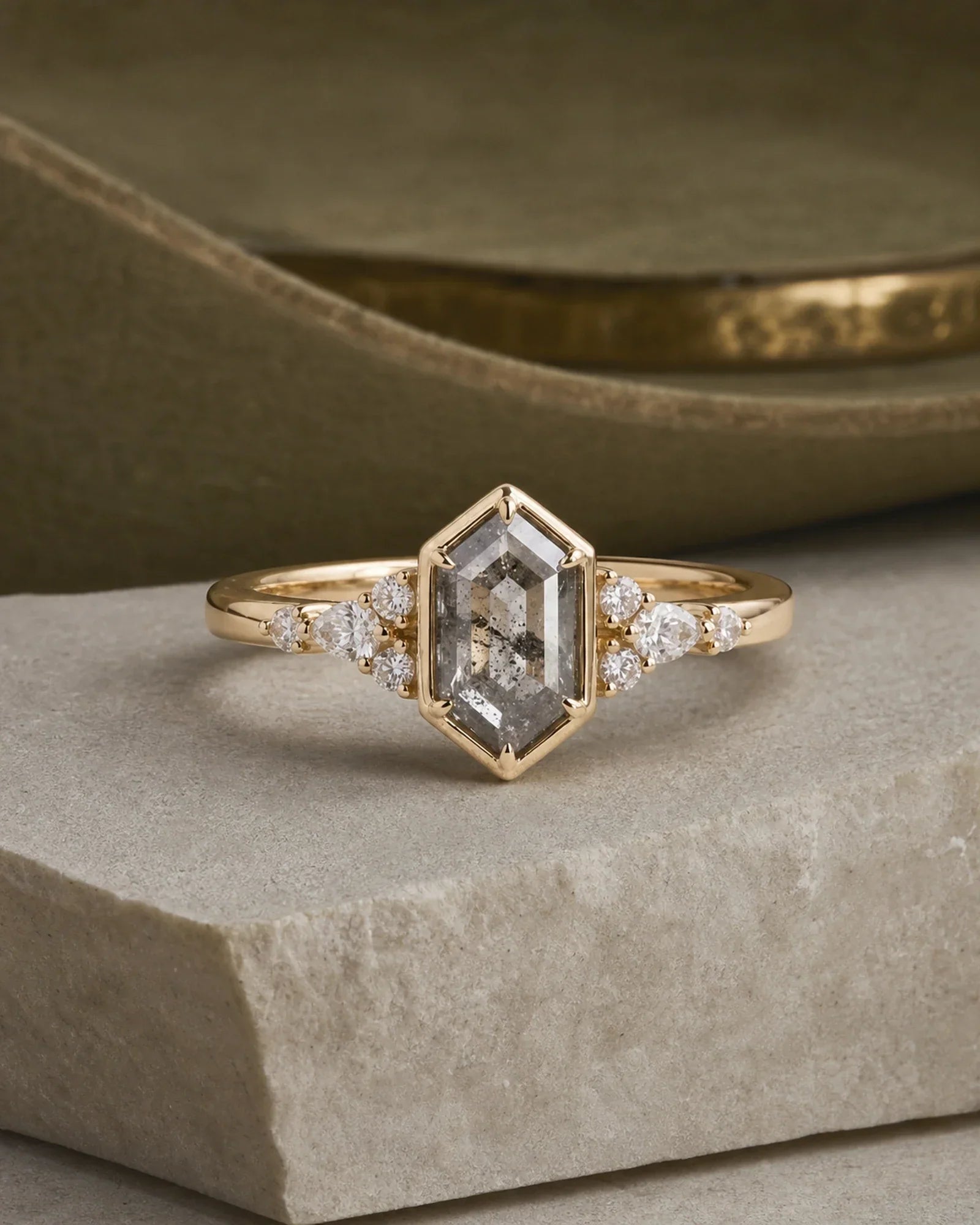 Hexagonal salt-and-pepper diamond bezel engagement ring on limestone with an olive suede backdrop