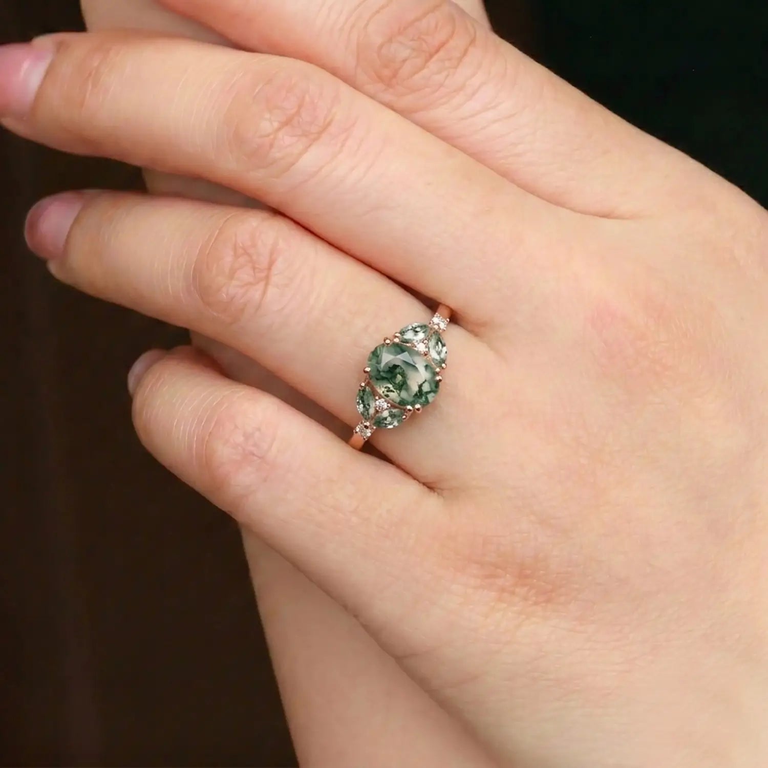 Woman wearing oval moss agate rose gold engagement ring with Art Deco cluster rings
