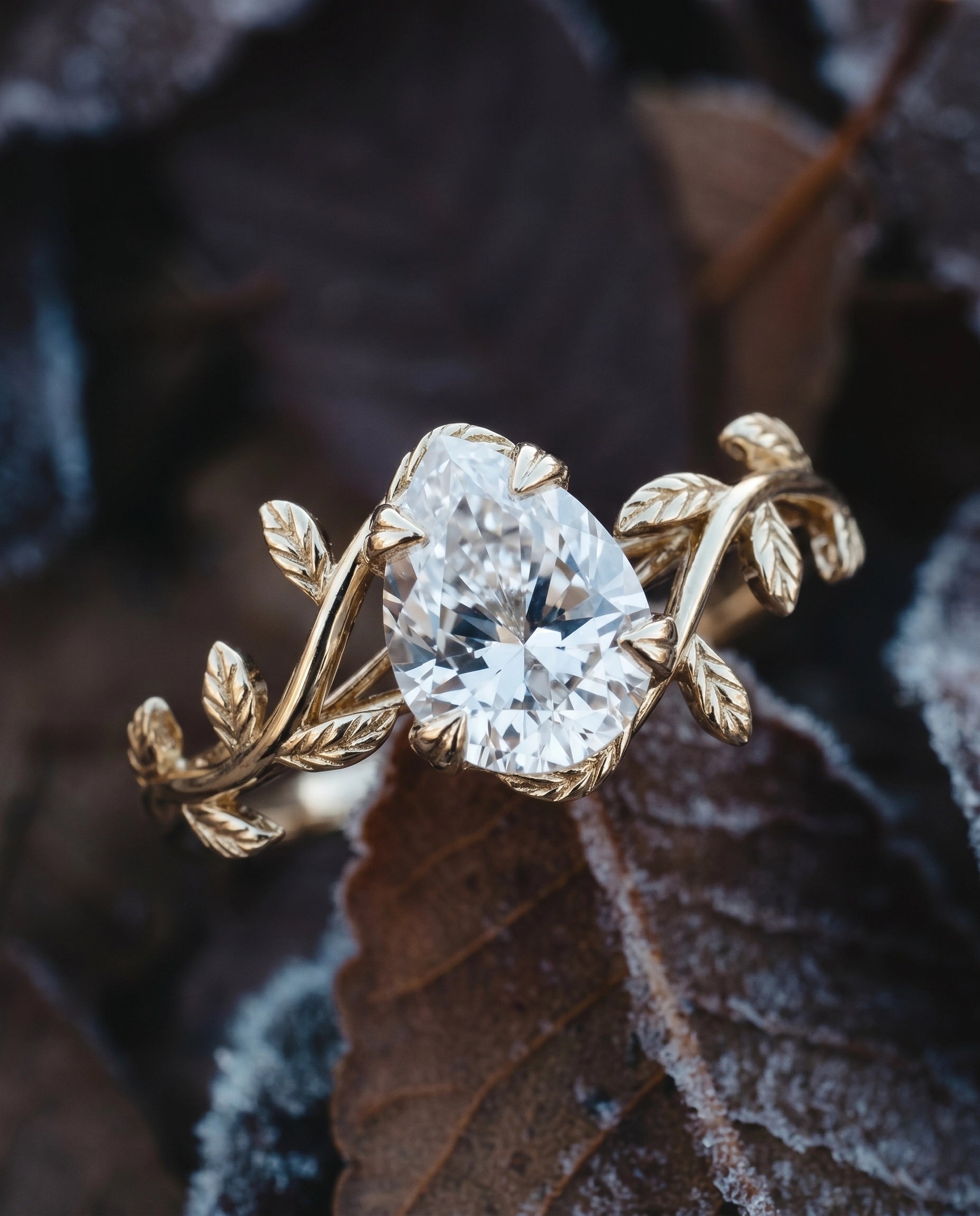A close-up shot of a nature-inspired, pear-cut moissanite solitaire ring, resting upon a leaf.