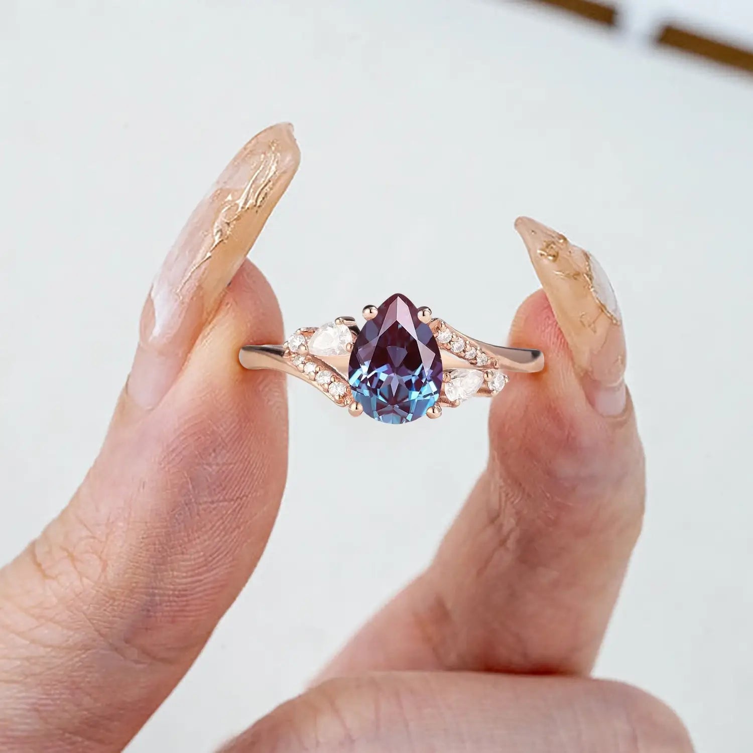 Woman wearing pear alexandrite rose gold engagement ring with moissanite cluster