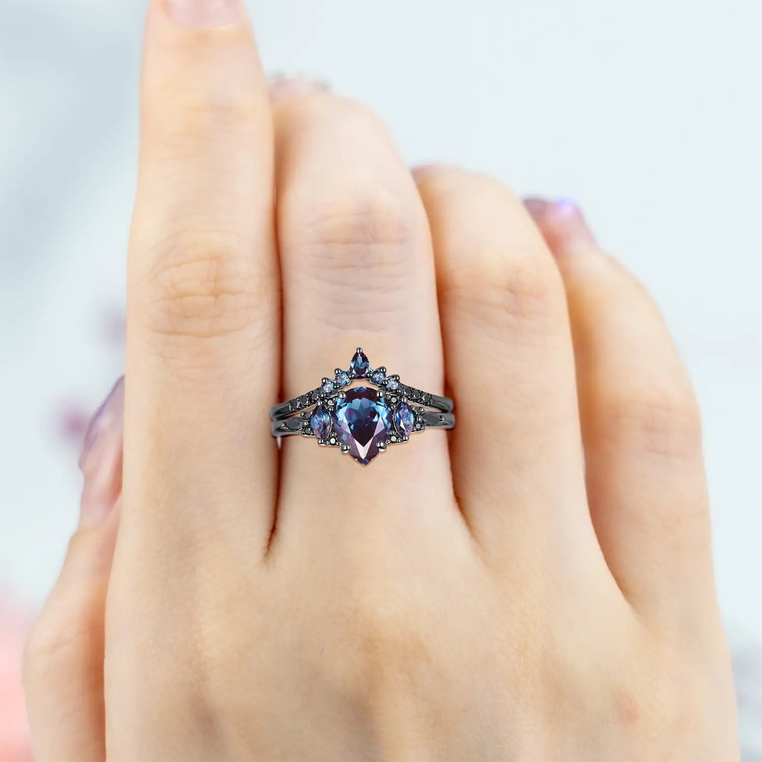 Woman wearing pear alexandrite engagement ring with black moissanite cluster and chevron wedding band showing color change