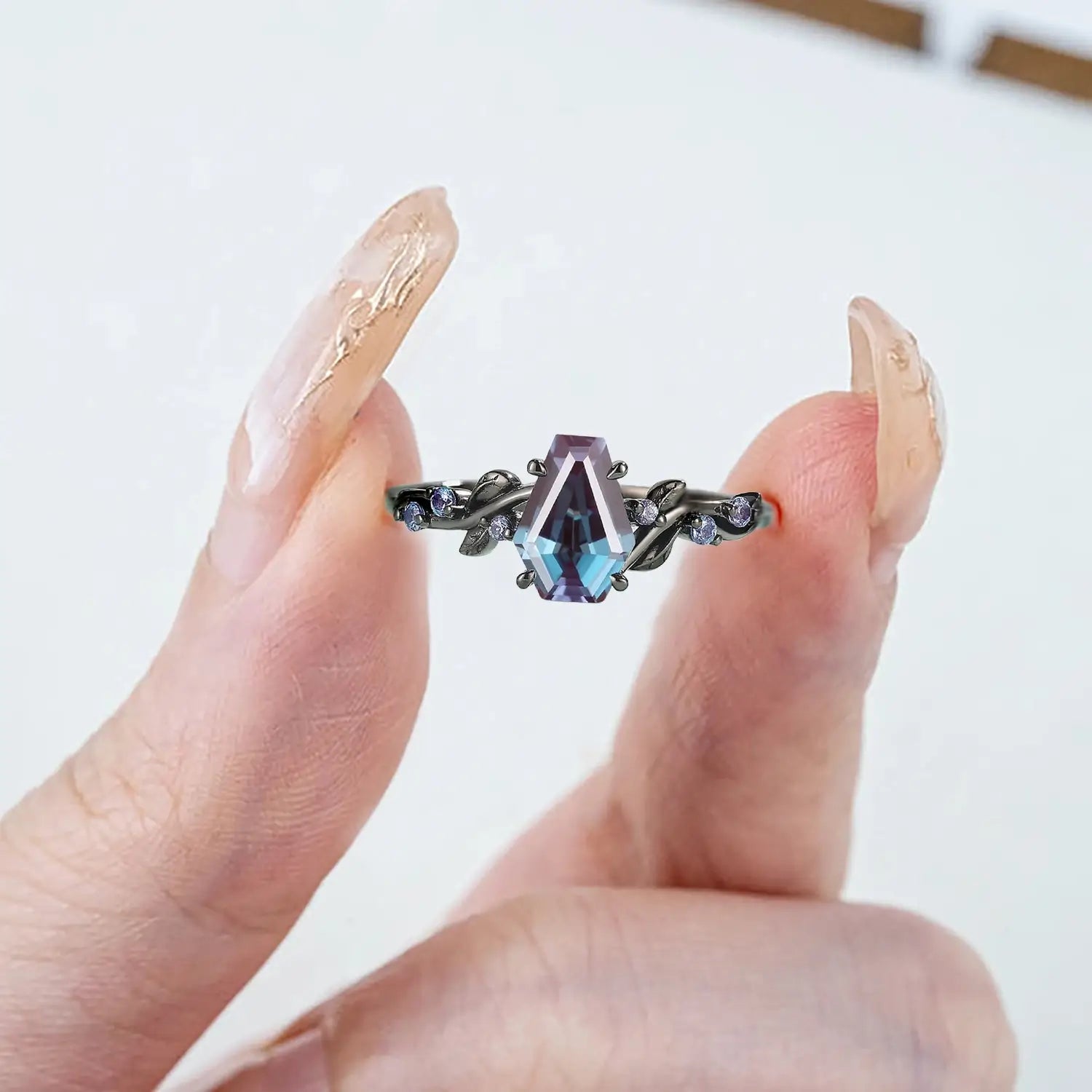 Woman wearing coffin alexandrite engagement ring with leaf band in black gold showing slender finger effect