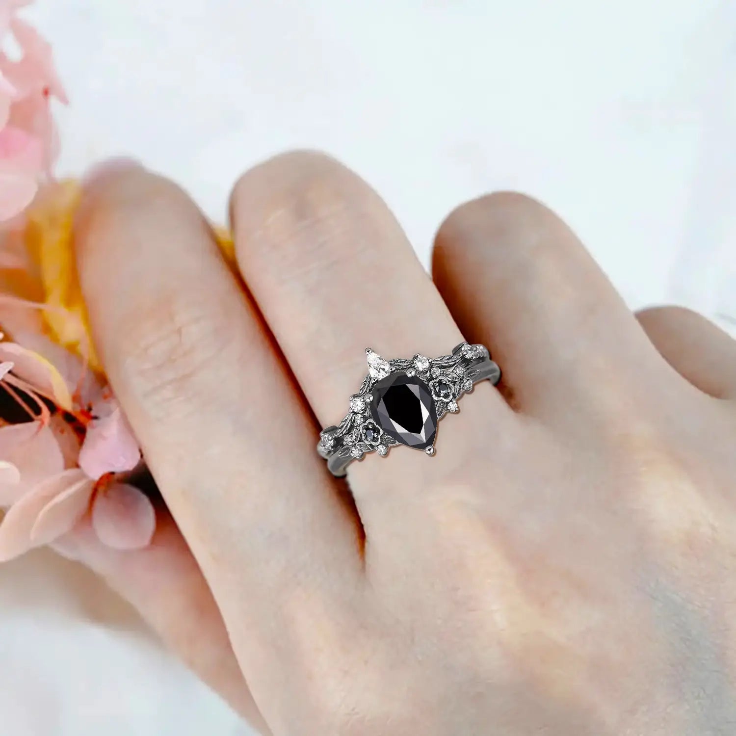 Woman wearing pear black onyx engagement ring with floral cluster and curved leaf wedding band in black gold