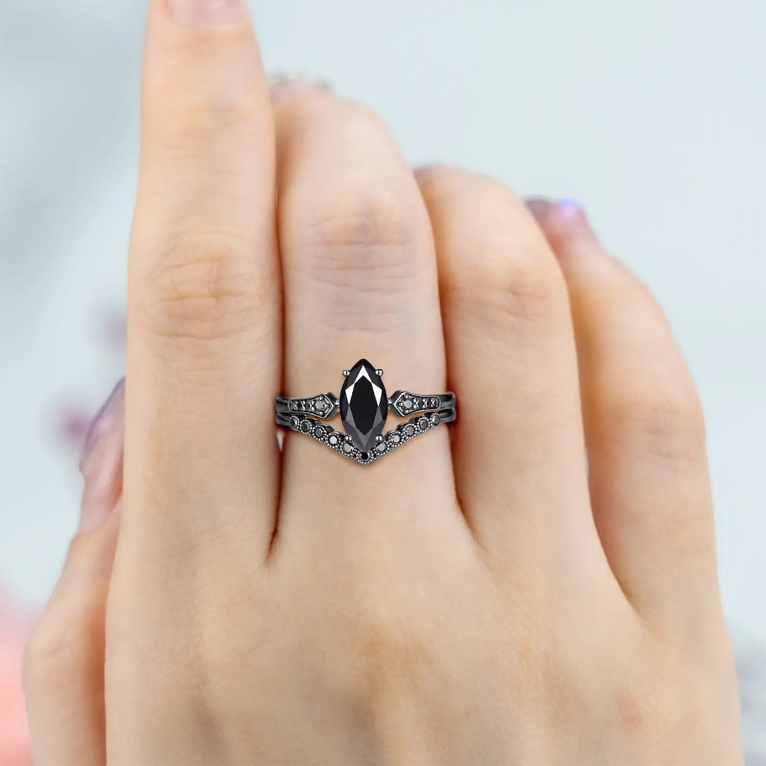 Woman wearing marquise black onyx engagement ring with vintage milgrain and chevron wedding band in black gold