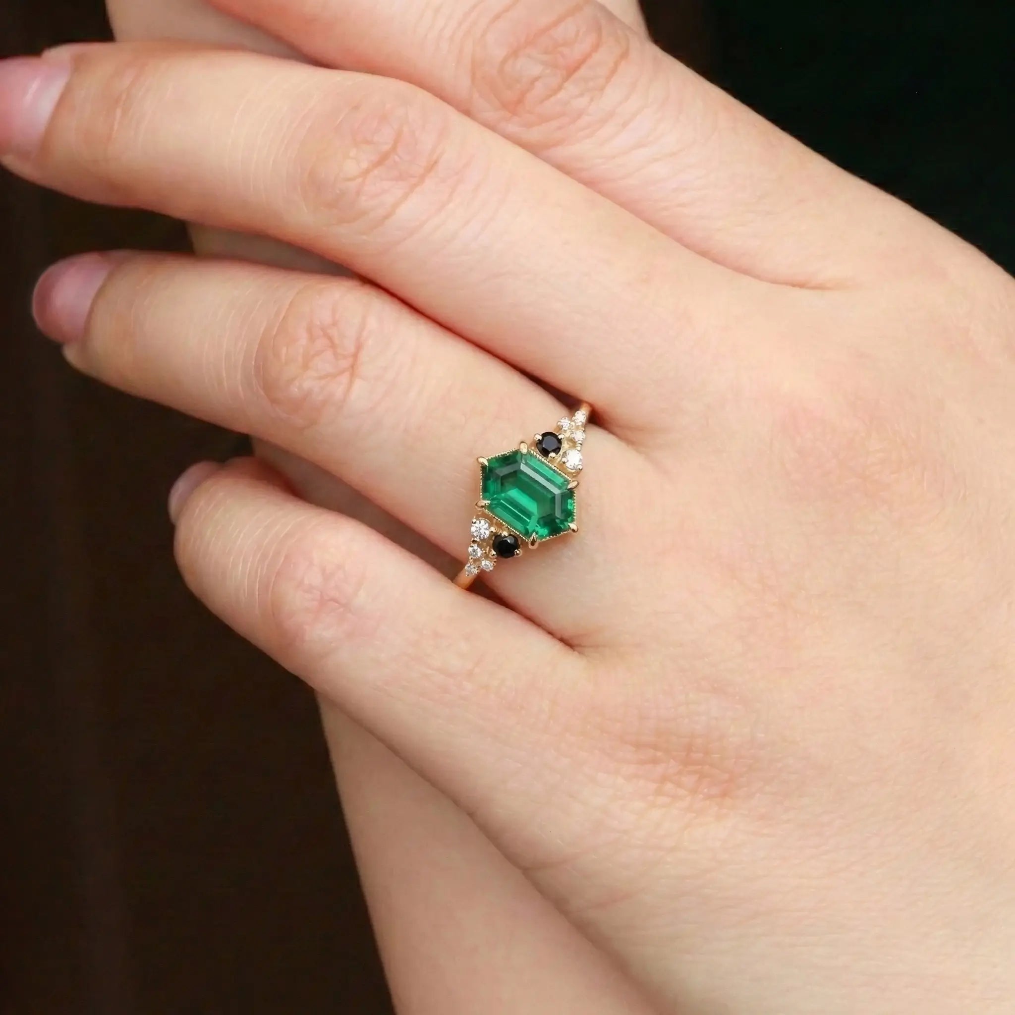 Woman wearing long hexagon emerald engagement ring in solid gold