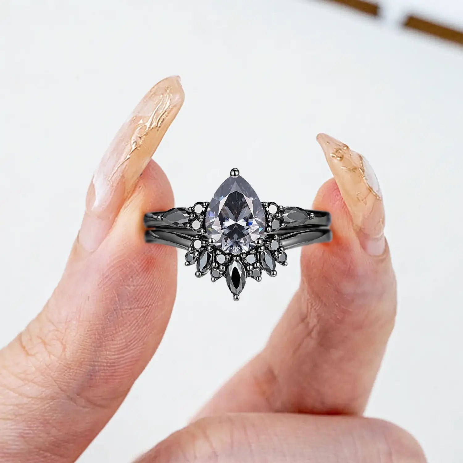 Woman wearing pear gray moissanite engagement ring with black moissanite cluster and onyx sunburst wedding band