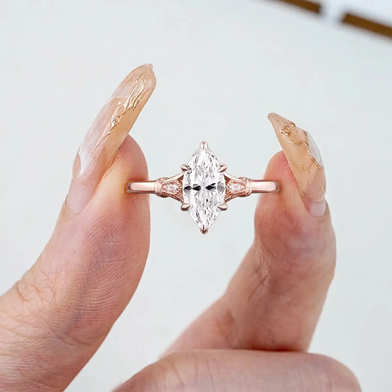 Woman wearing marquise moissanite engagement ring with pear accents on vintage split shank rose gold band