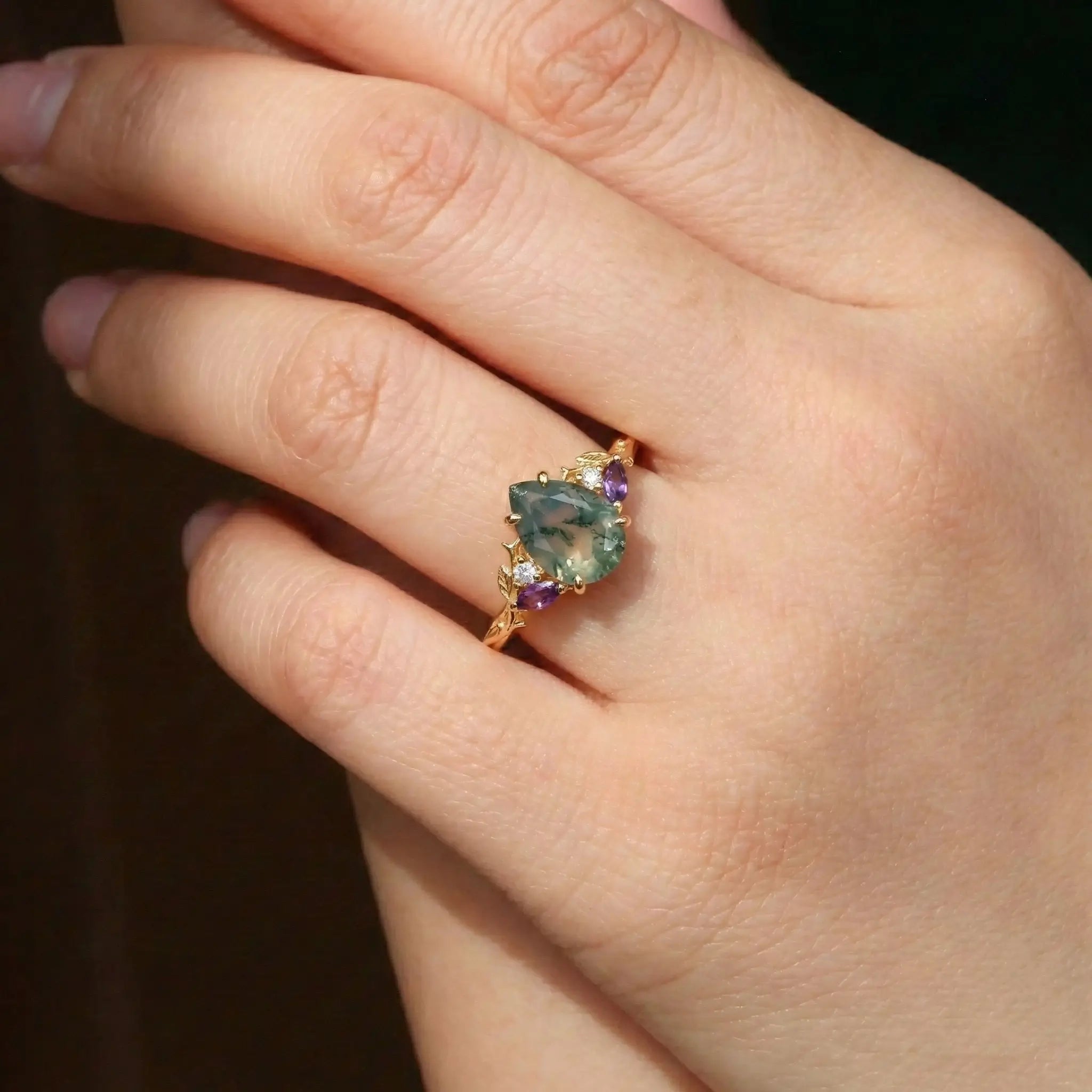 Woman wearing pear cut moss agate engagement ring with leaf gold band