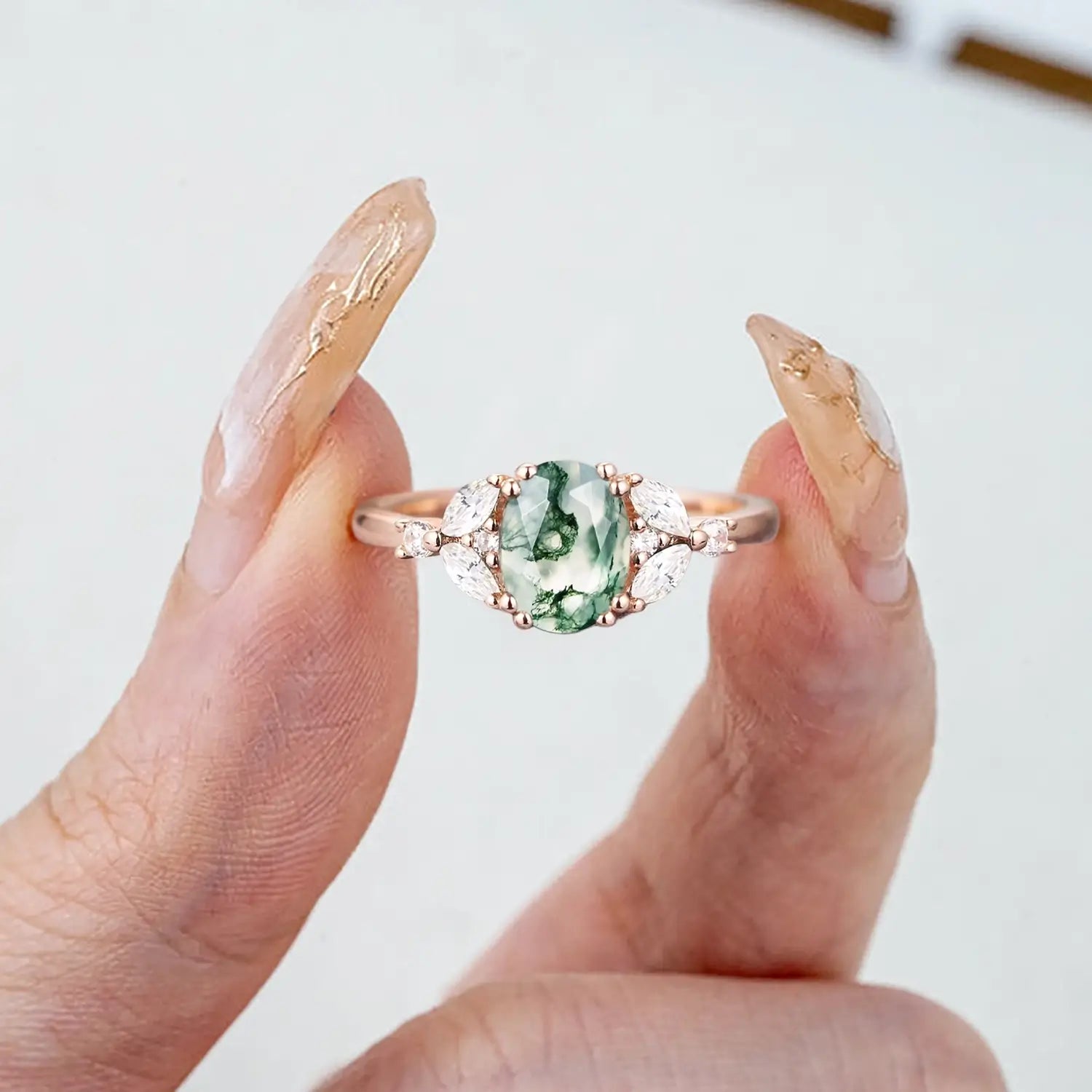 Woman wearing oval moss agate rose gold engagement ring with pear diamond cluster