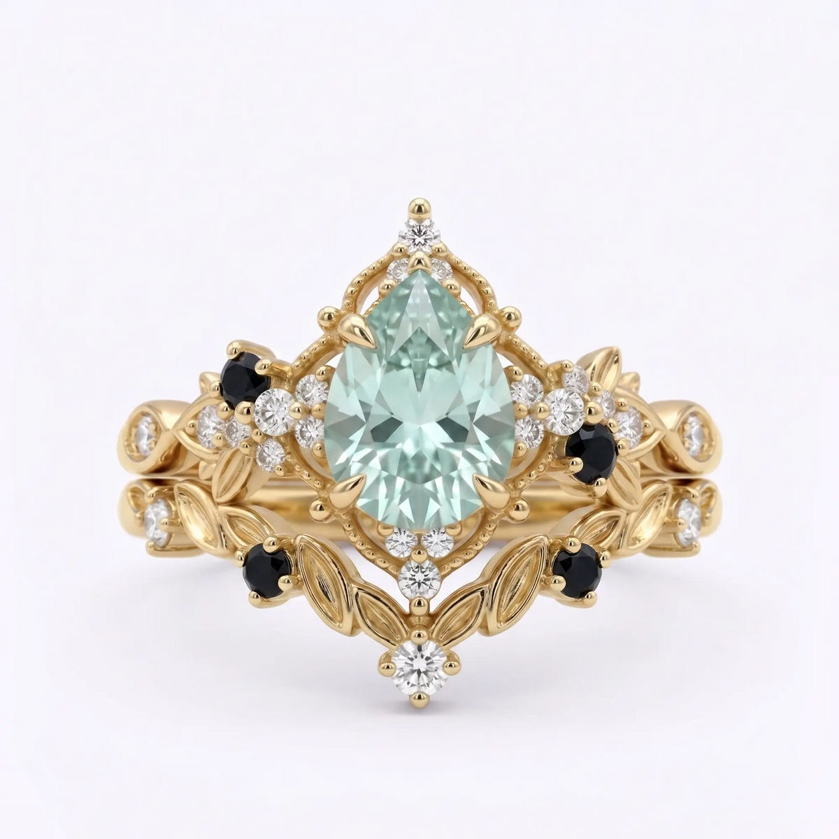 Handcrafted alternative bridal pear-cut grey moissanite engagement ring stacked with a matching black onyx and moissanite leafy wedding band in solid yellow gold by Orleon