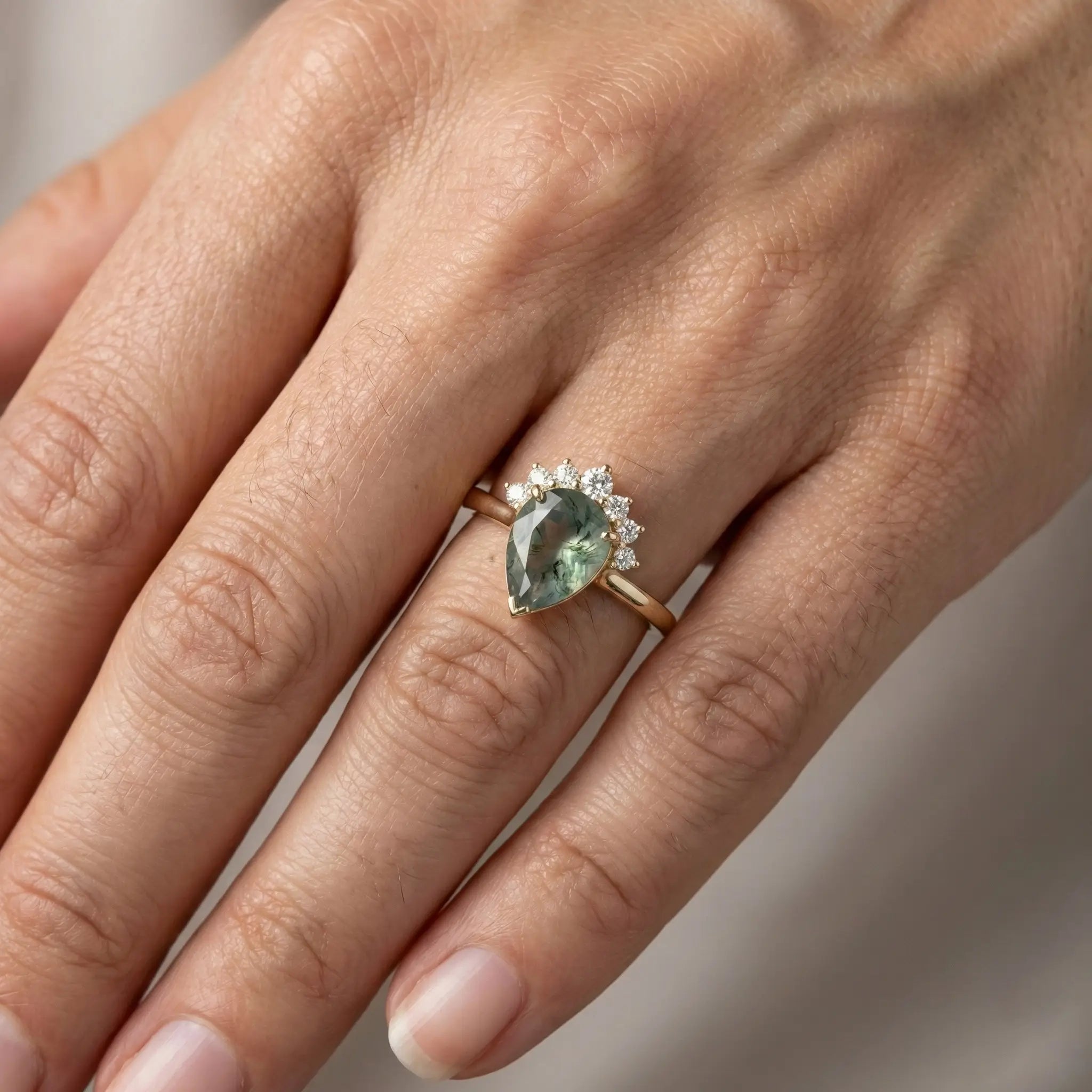 Woman wearing pear moss agate yellow gold engagement ring with half-halo crown