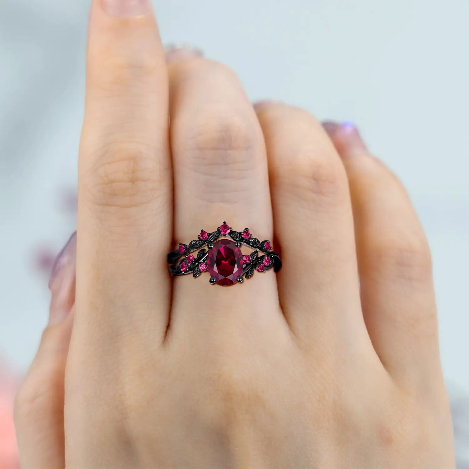 Woman wearing oval ruby engagement ring with black gold leaf band and wedding ring set