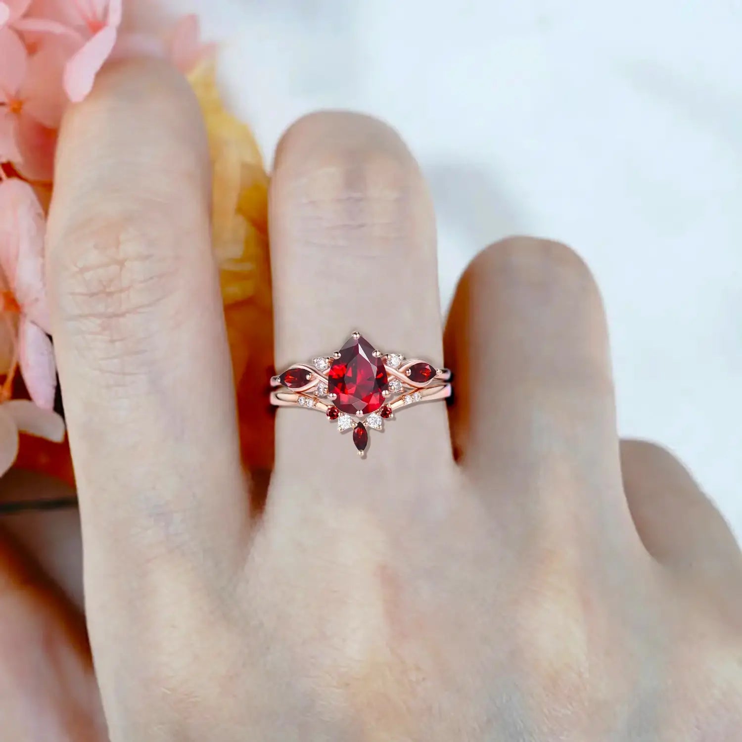 Woman wearing pear ruby engagement ring with marquise cluster and V shaped wedding band in rose gold