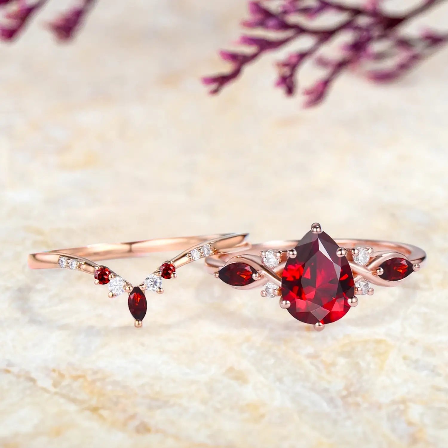Pear ruby marquise cluster engagement ring and V shaped wedding band displayed separately showing July birthstone bridal set