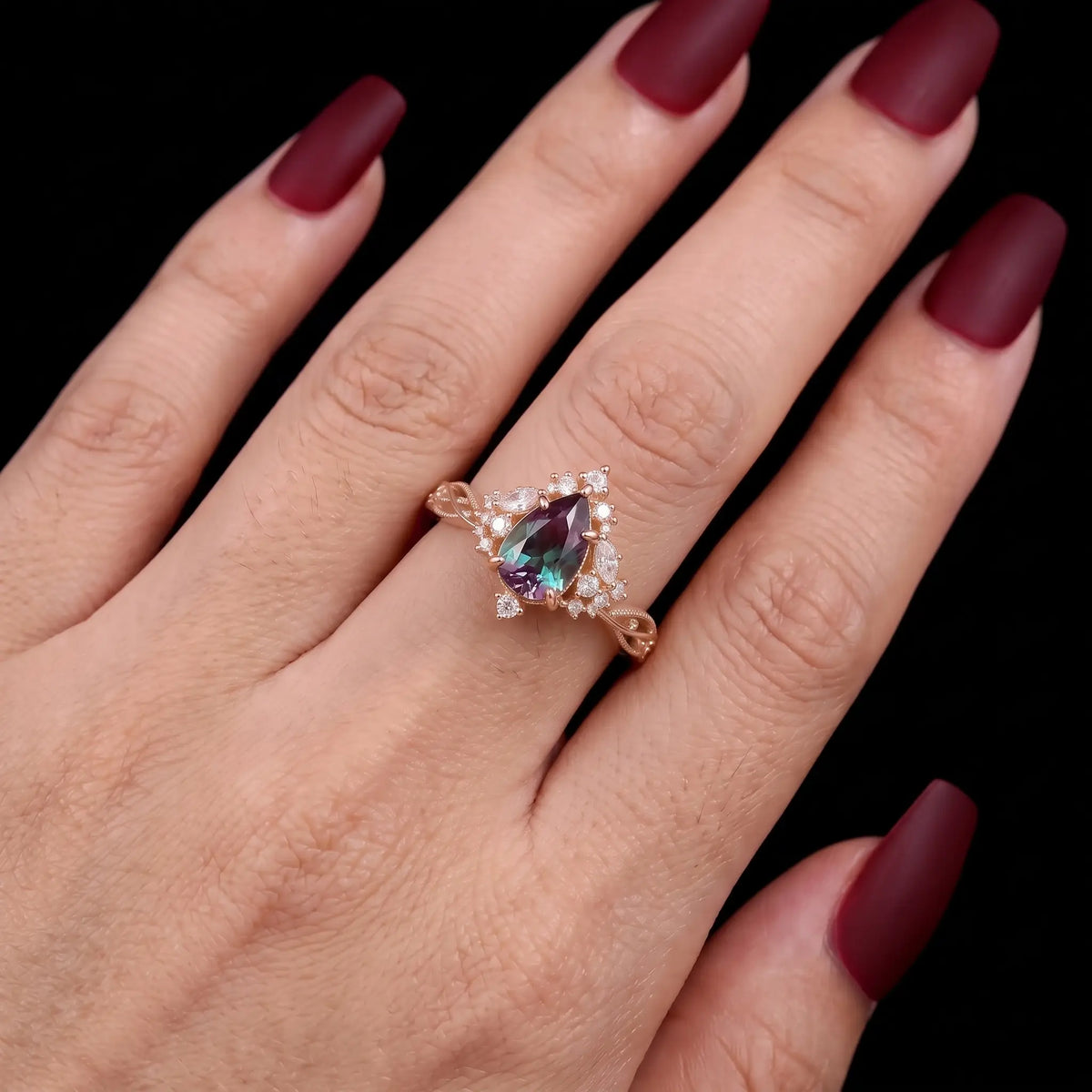 Selviora pear cut lab alexandrite engagement ring worn on a finger, displaying its color-changing gemstone, delicate cluster halo and romantic twisted gold band.