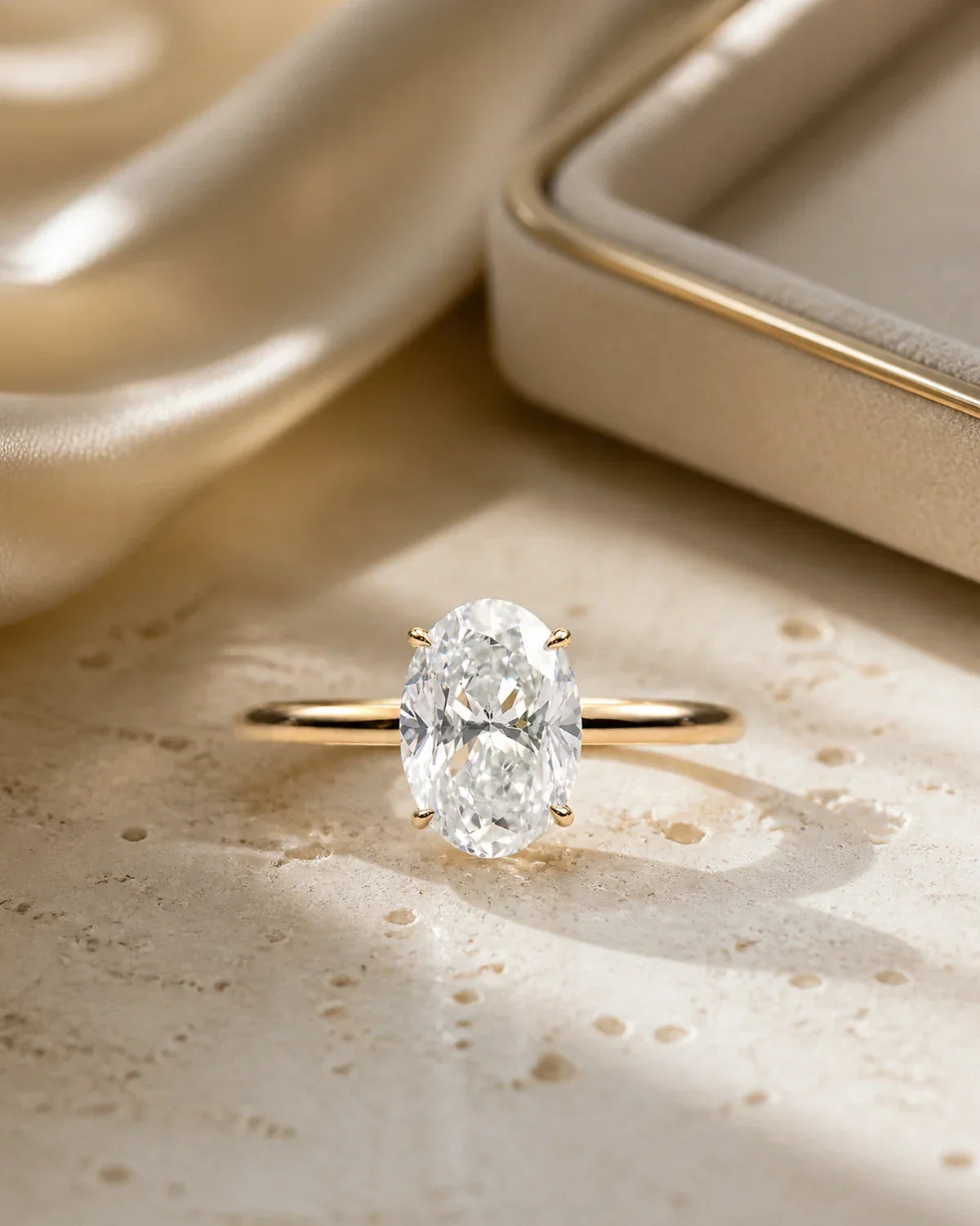 Modern oval hidden halo ring on warm stone and champagne silk