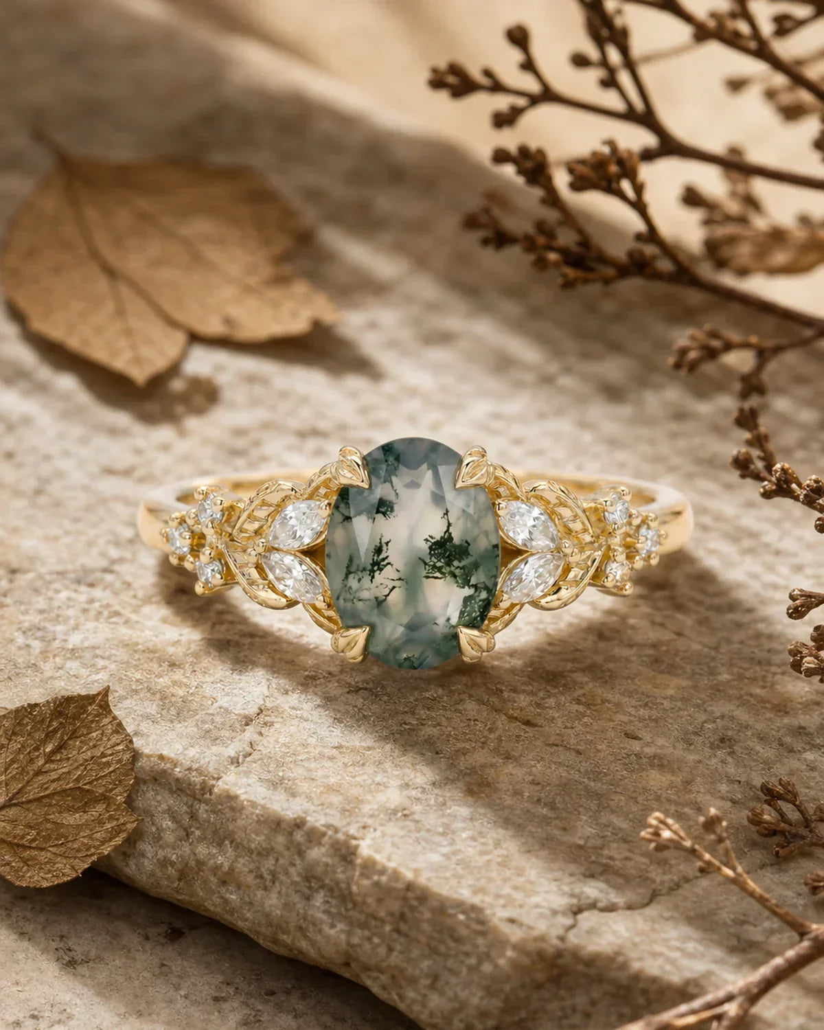 Moss agate leaf engagement ring on stone with dried twigs and pressed leaves