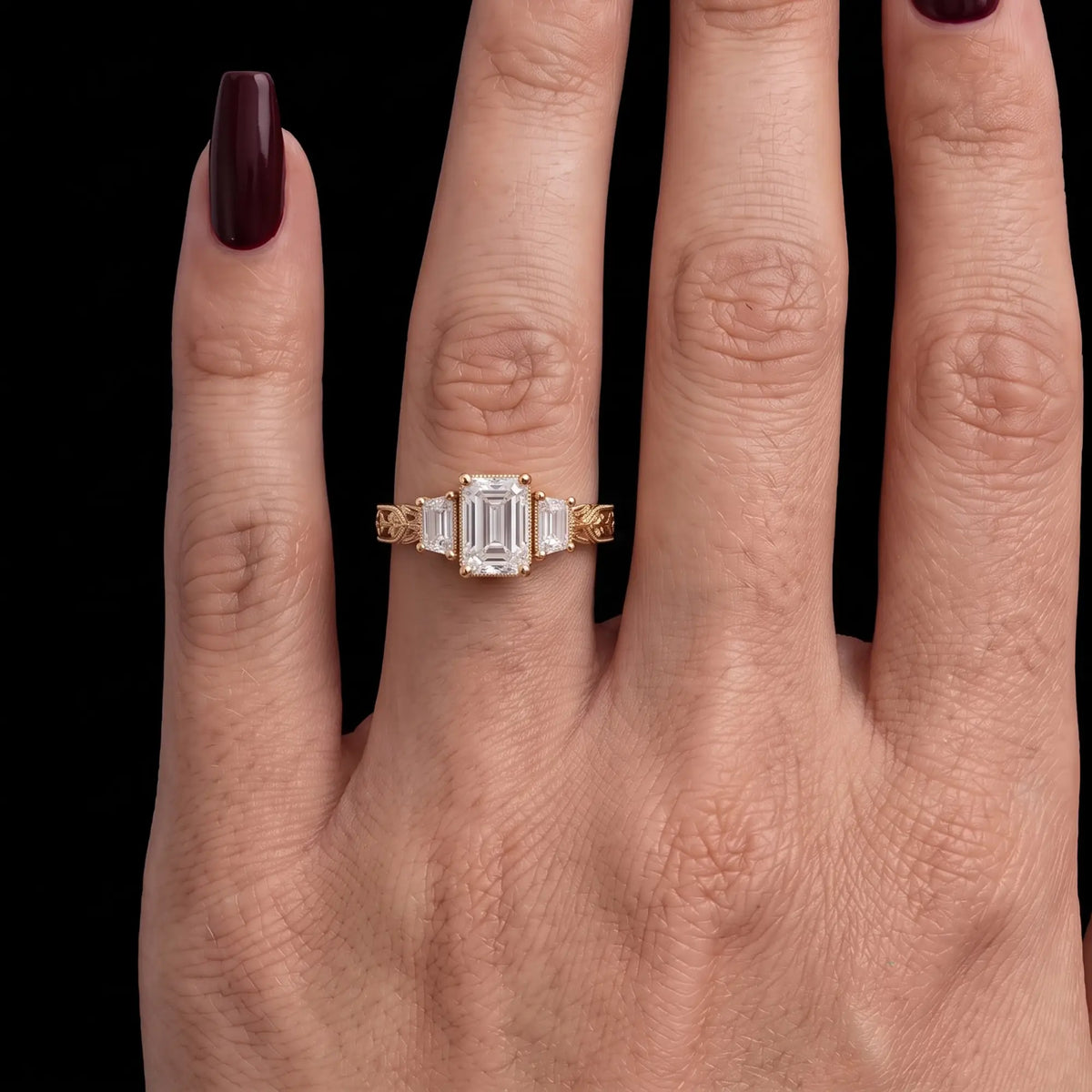 Emerald cut moissanite three stone engagement ring with leaf filigree band worn on hand
