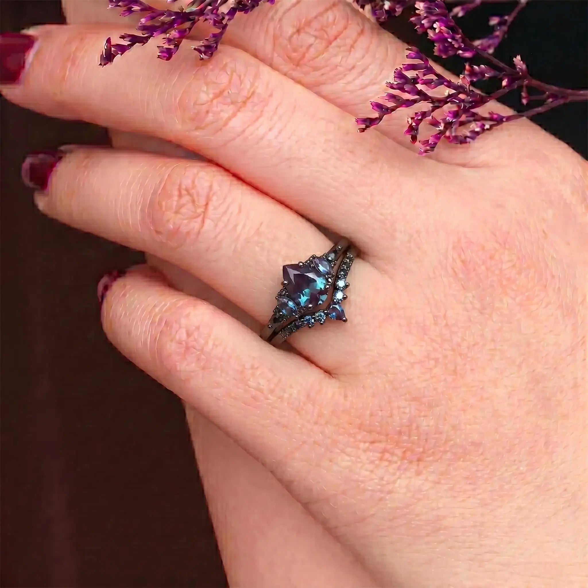 Woman wearing pear alexandrite engagement ring with black moissanite cluster and chevron wedding band showing color change