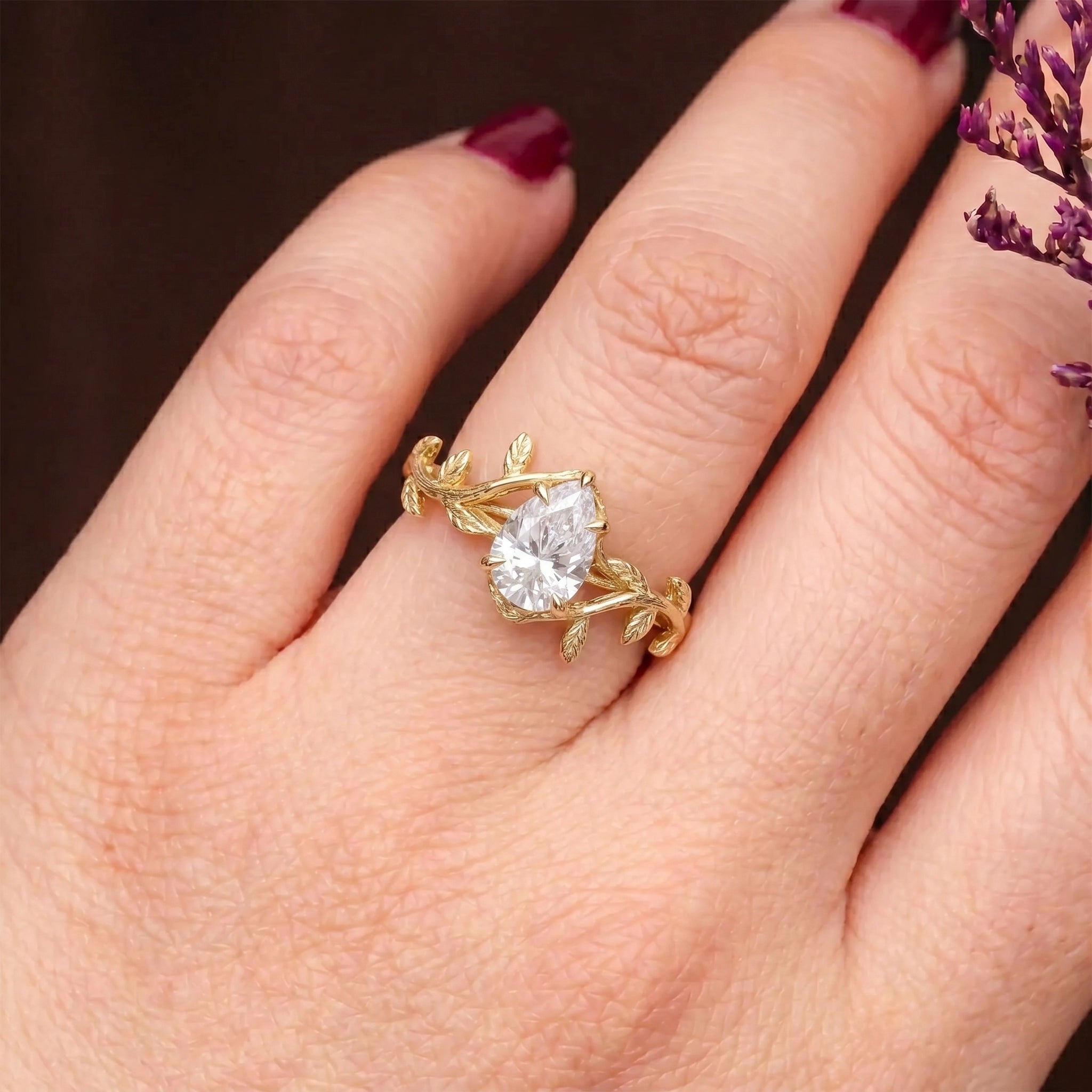 The hand of a sophisticated woman, adorned with a custom-made Orleone ring—an 18K gold, pear-cut solitaire featuring a nature-inspired moissanite