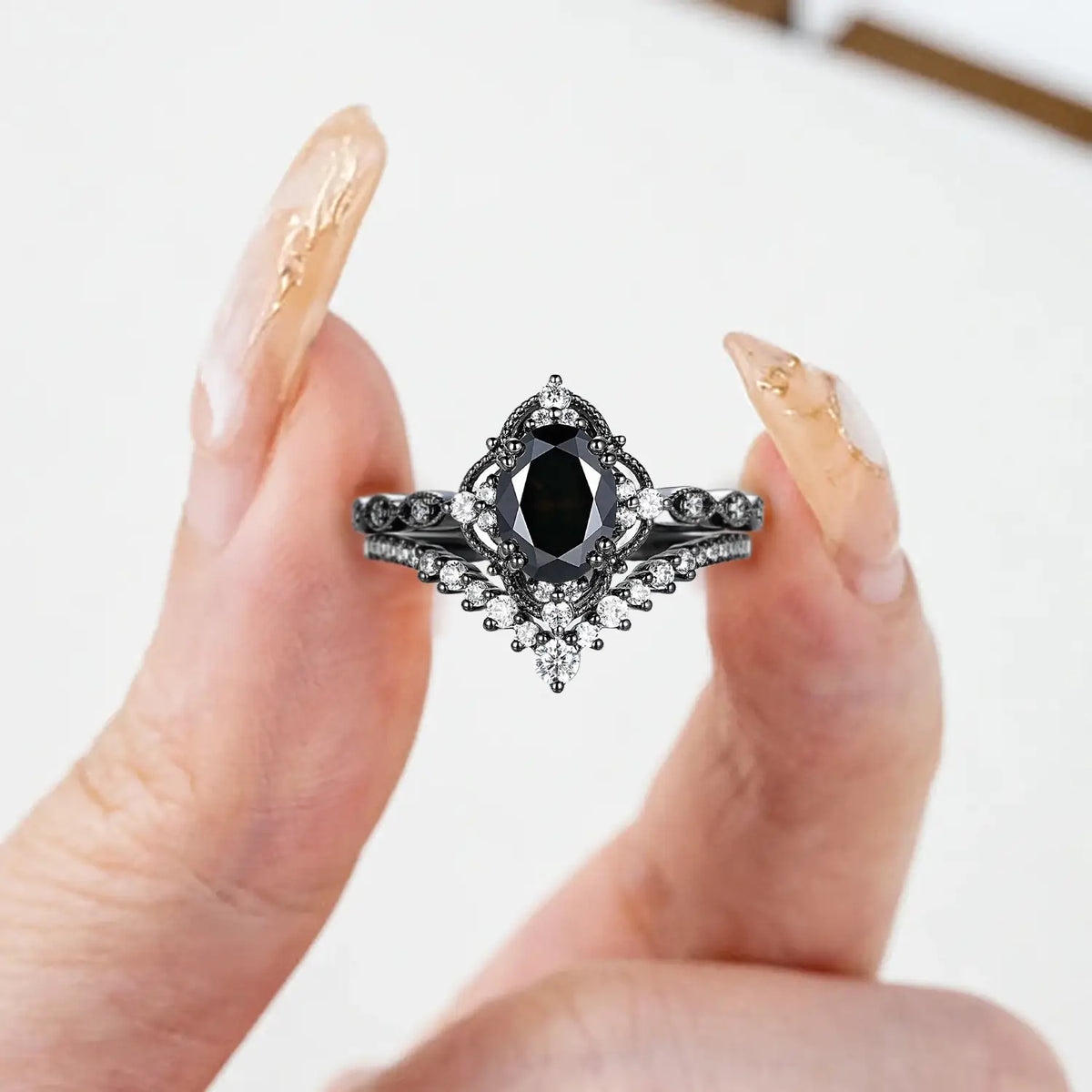 Woman wearing oval black onyx engagement ring with crown cluster and chevron wedding band in black gold