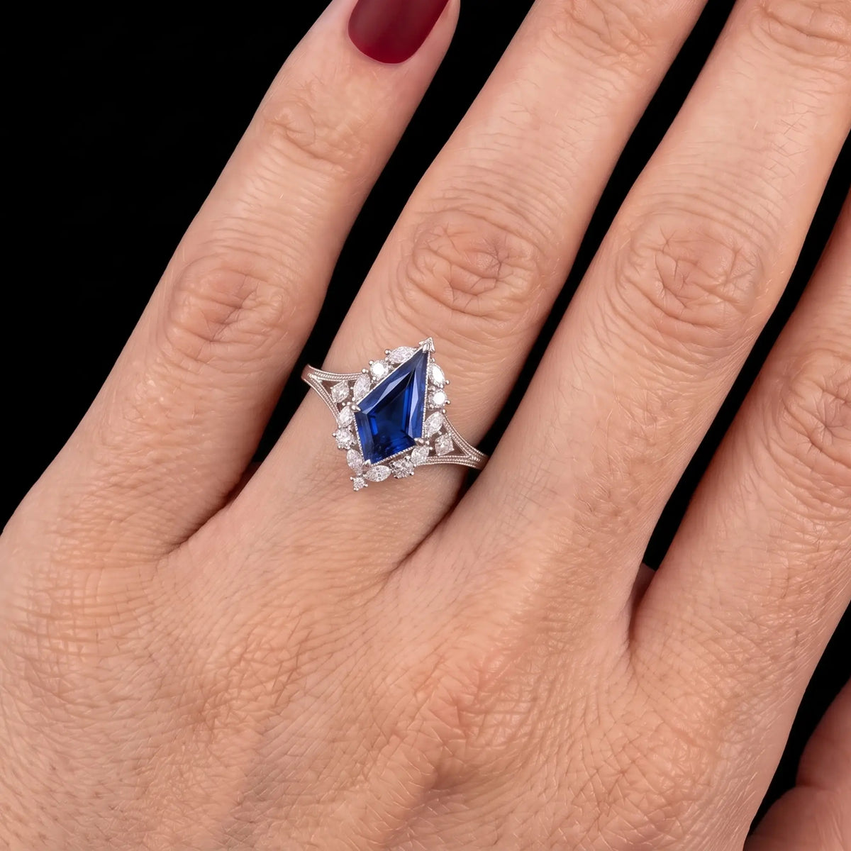 Elarisse royal blue kite cut lab sapphire engagement ring worn on a finger, showing the elongated gemstone, ornate halo setting and delicate vintage band.