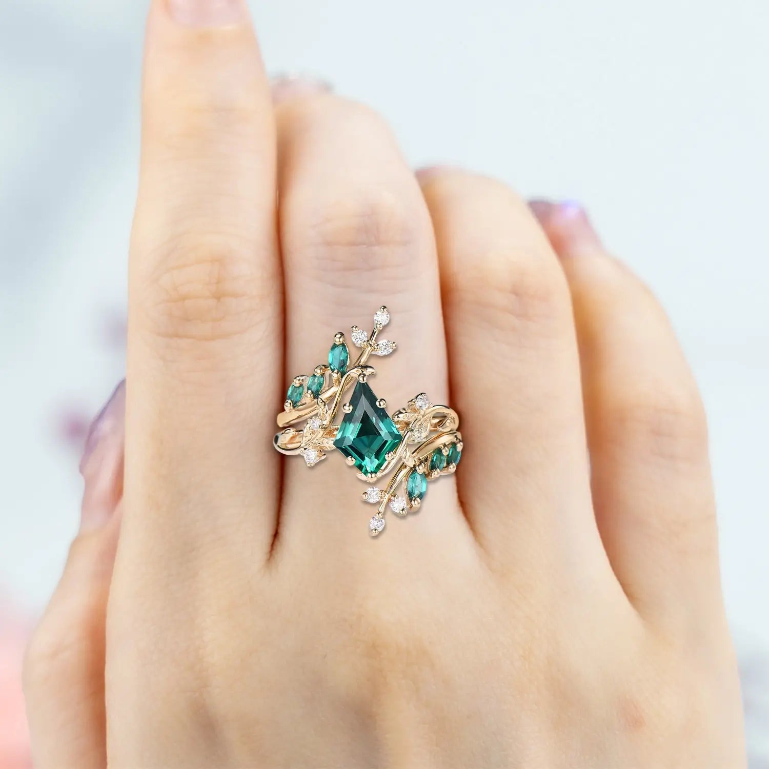 Woman wearing kite emerald yellow gold engagement ring set with leafy clusters
