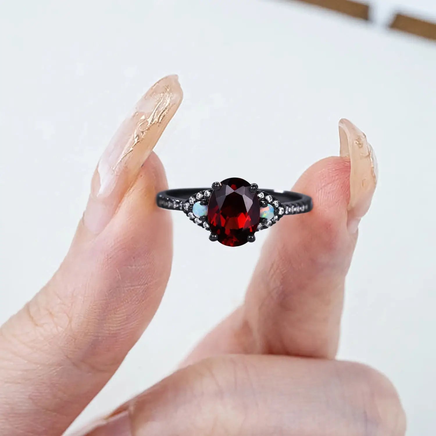 Woman wearing oval garnet black gold engagement ring with opal accents