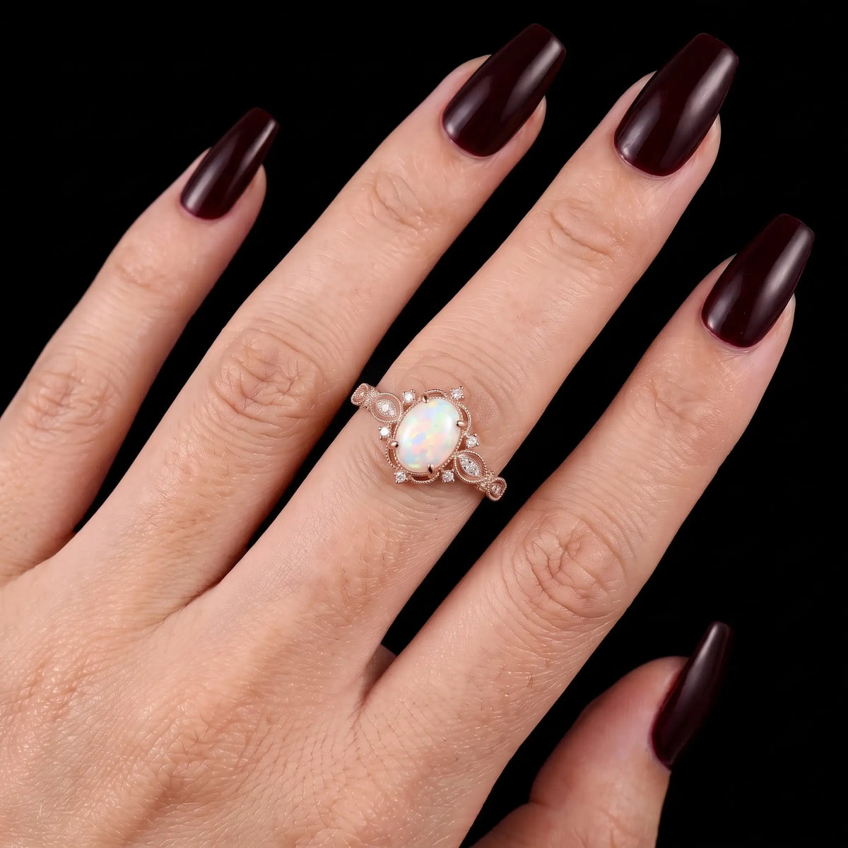 Iravelle oval white opal engagement ring worn on a finger, showing the romantic Edwardian filigree design and delicate rose gold band.