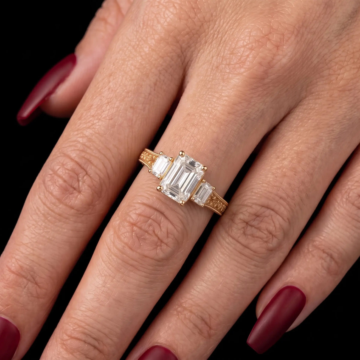 Vintage emerald cut lab diamond three stone engagement ring worn on hand with delicate filigree gold shoulders