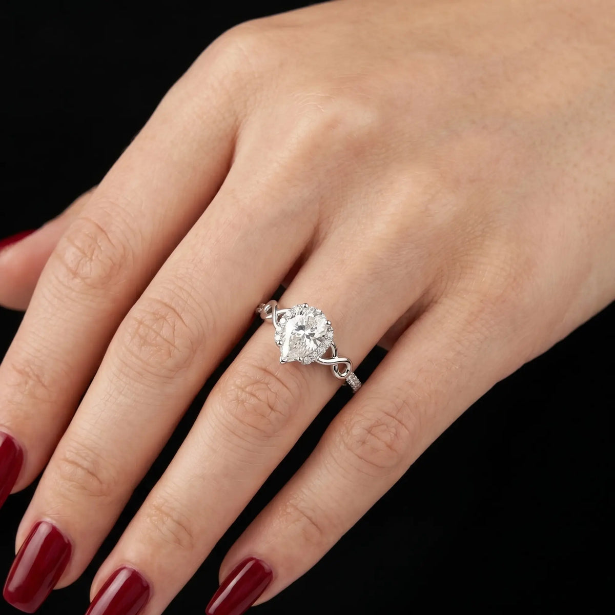 Luminous handmade pear cut moissanite halo ring on hand showing intricate infinity loop shoulders