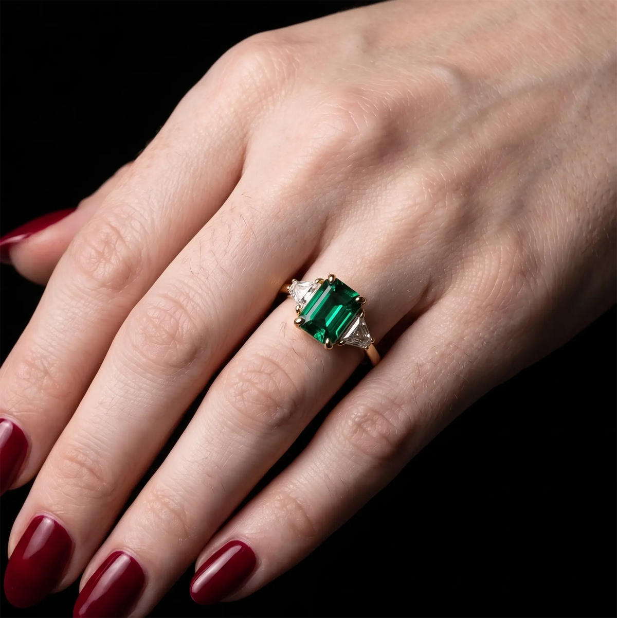 Emerald cut emerald three stone ring worn on hand with timeless gold design