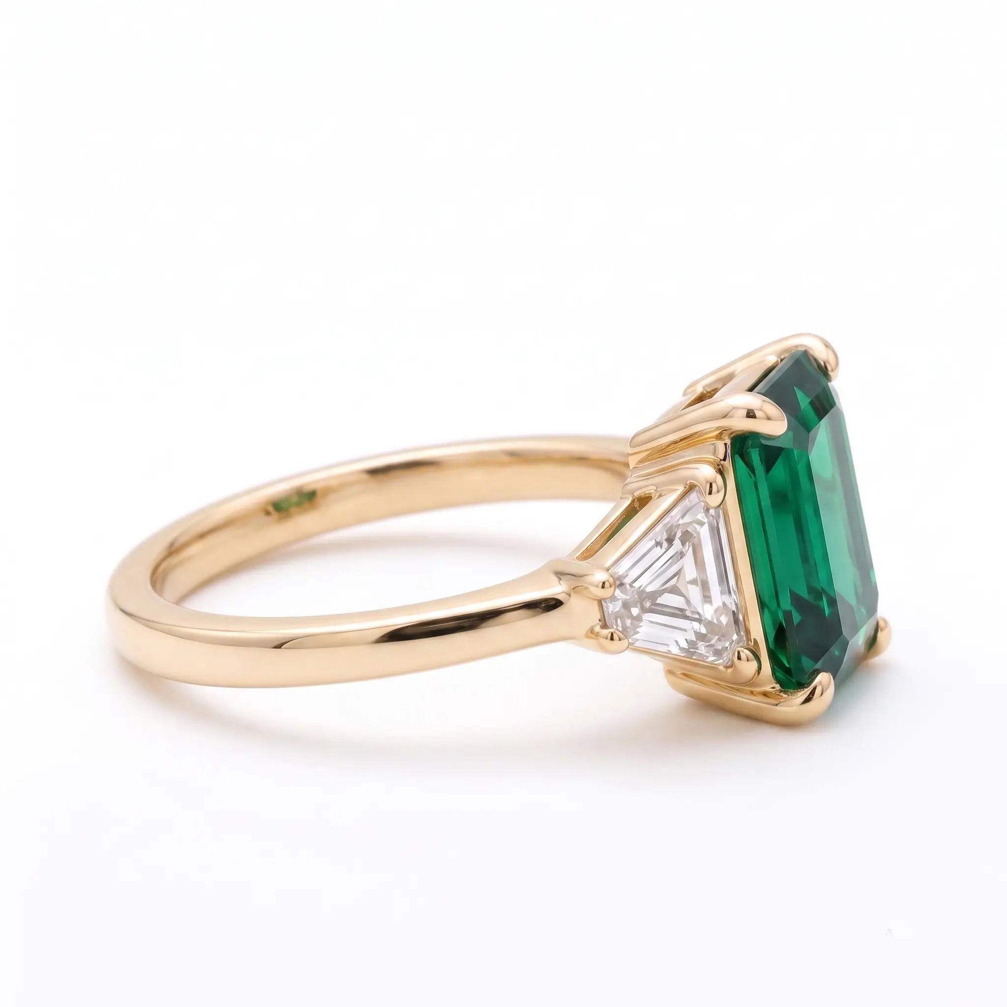 Side view of classic emerald three stone ring with slim gold band