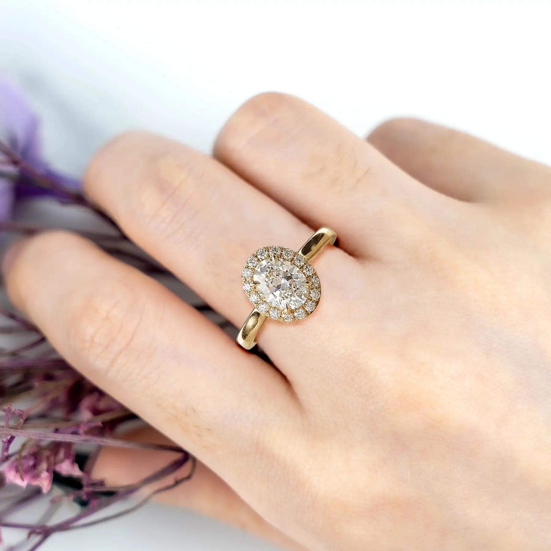 Woman wearing oval moissanite yellow gold halo engagement ring classic style