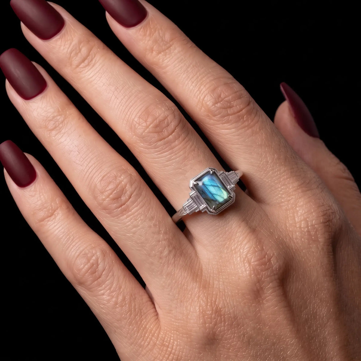 Natural blue flash emerald cut labradorite engagement ring worn on hand with vintage Art Deco white gold details