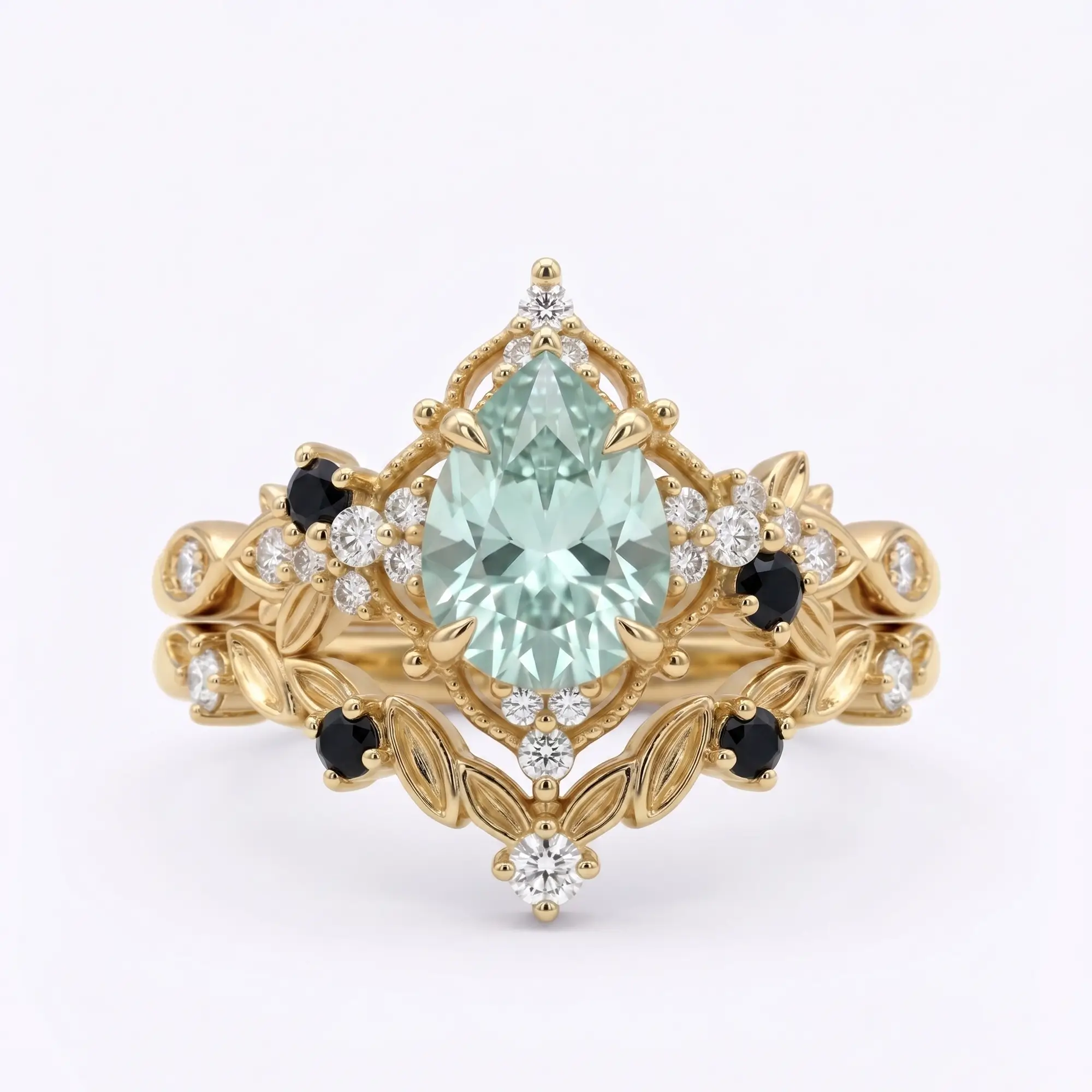 Handcrafted alternative bridal pear-cut grey moissanite engagement ring stacked with a matching black onyx and moissanite leafy wedding band in solid yellow gold by Orleon