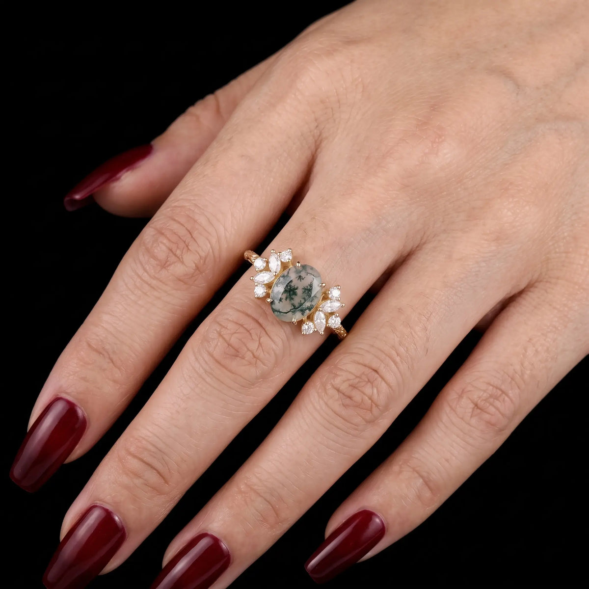 Oval moss agate engagement ring worn on hand with elegant cluster silhouette