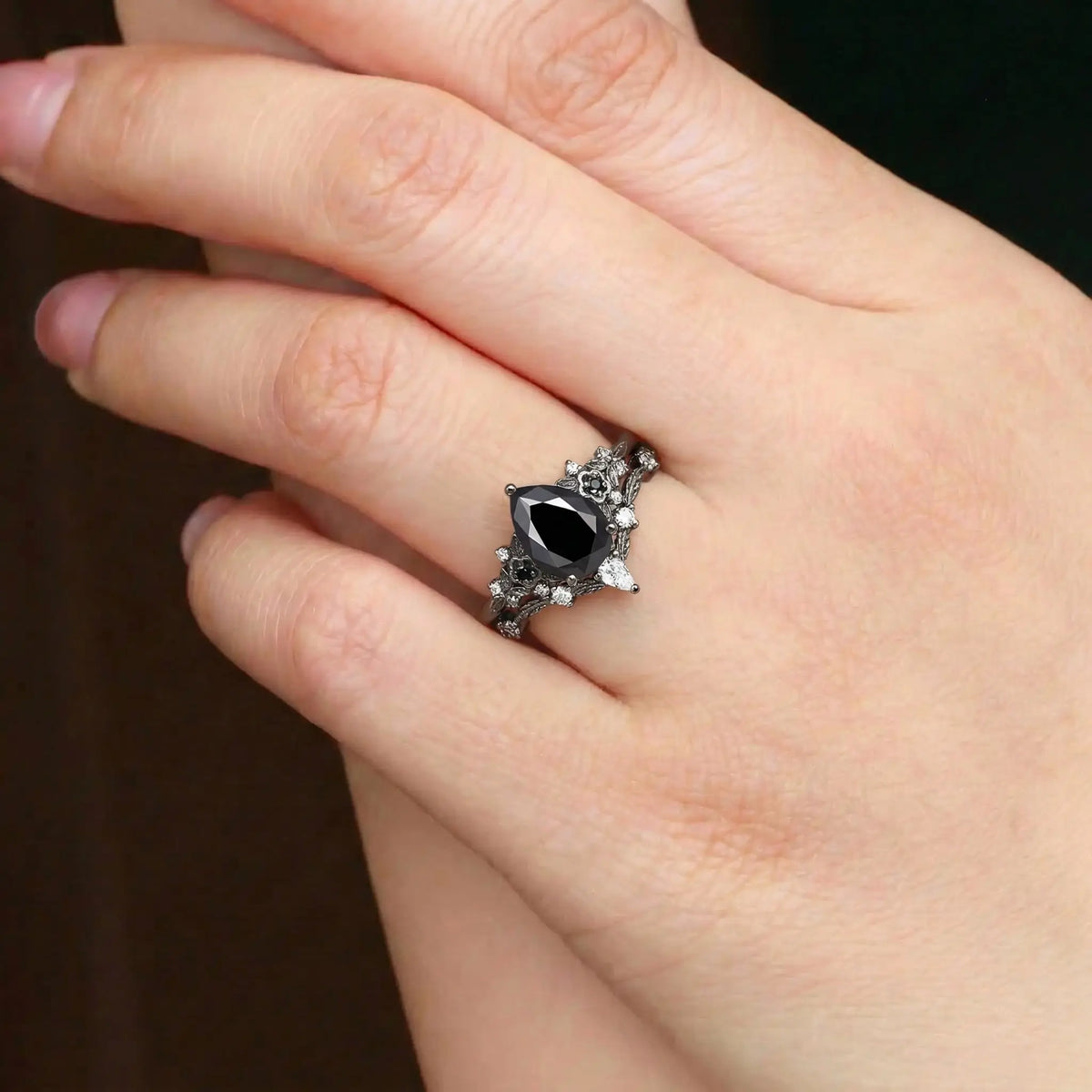 Woman wearing pear black onyx engagement ring with floral cluster and curved leaf wedding band in black gold