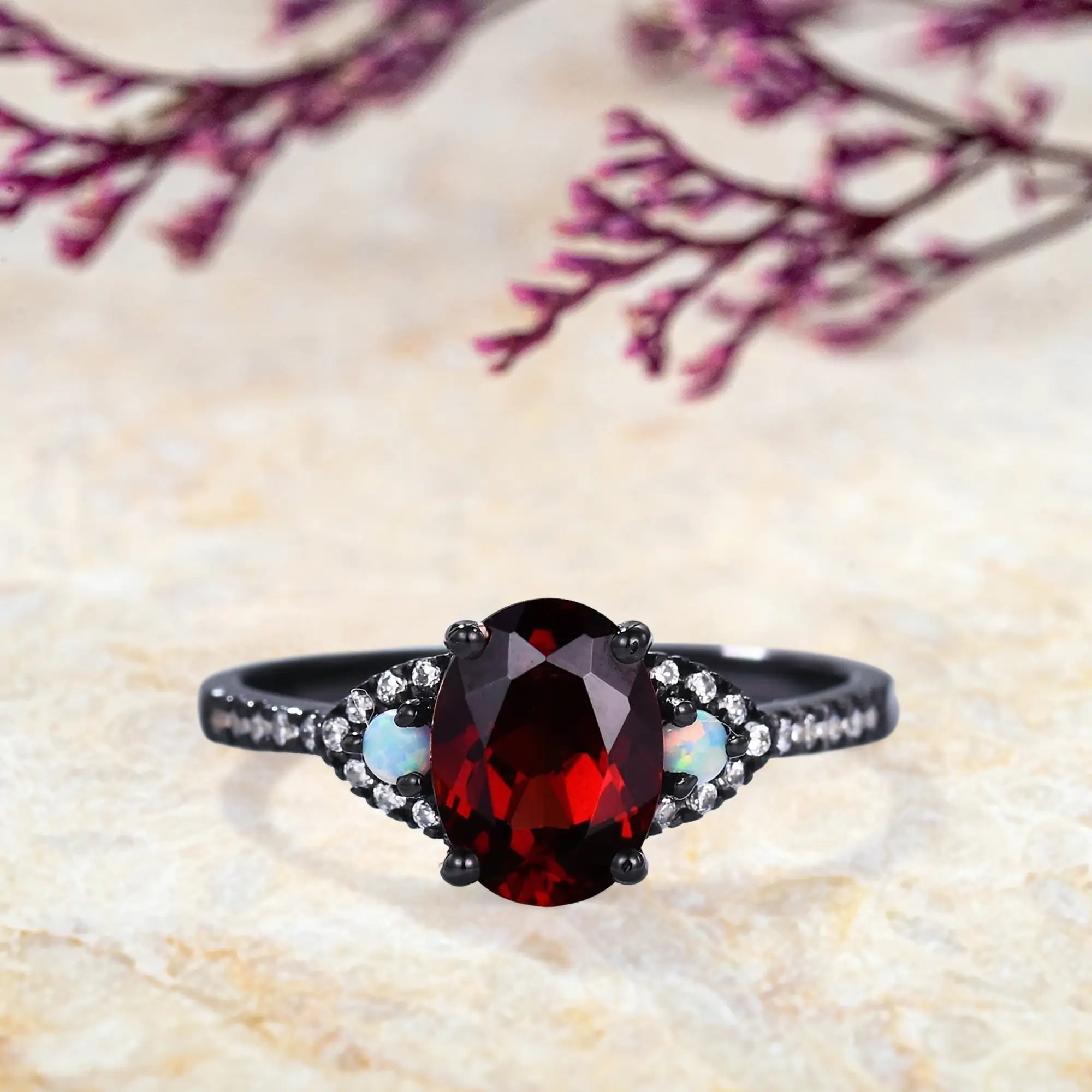 Oval garnet engagement ring in black gold with opal side stones Gothic three-stone design
