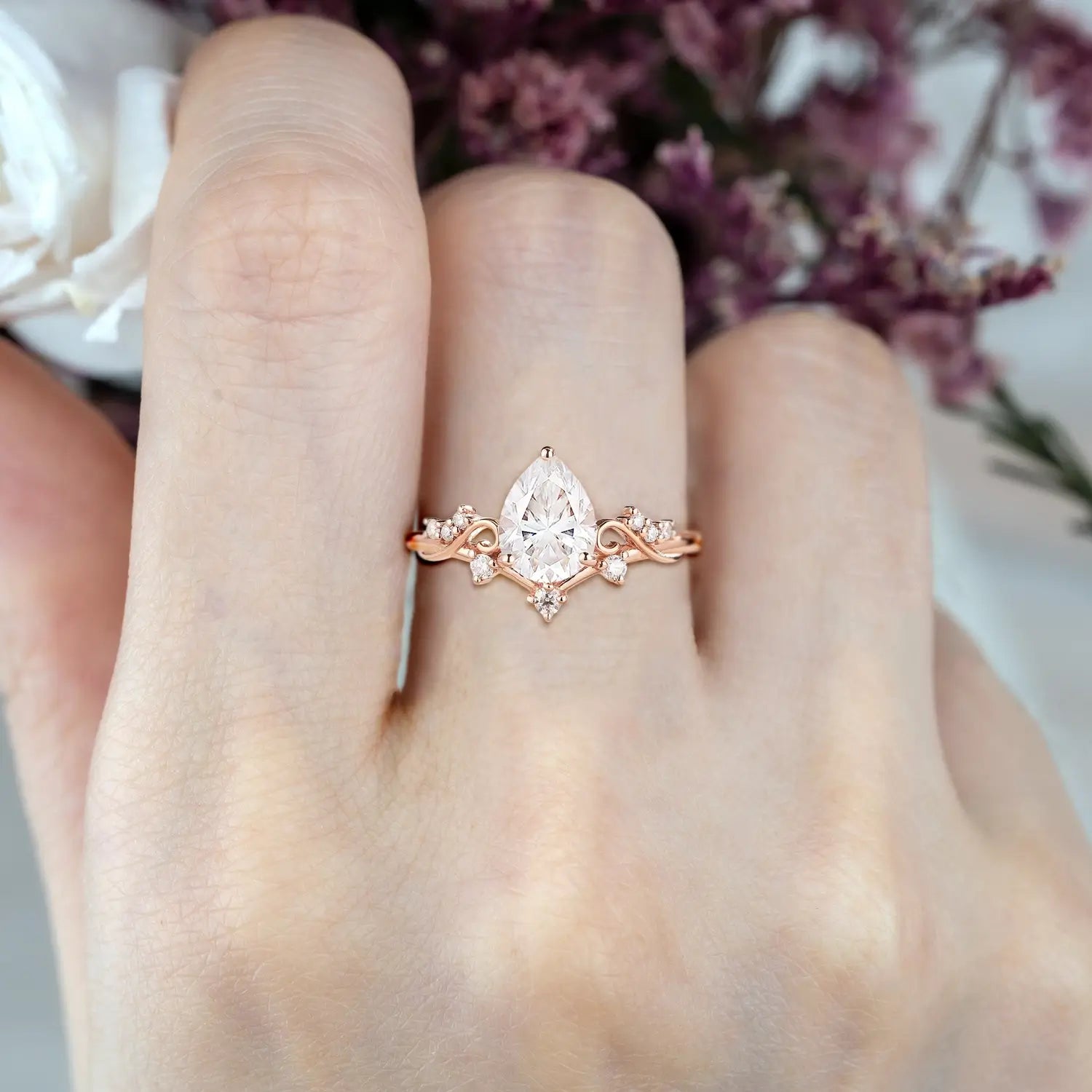 Woman wearing pear shaped moissanite engagement ring with vintage cluster and curved rose gold band