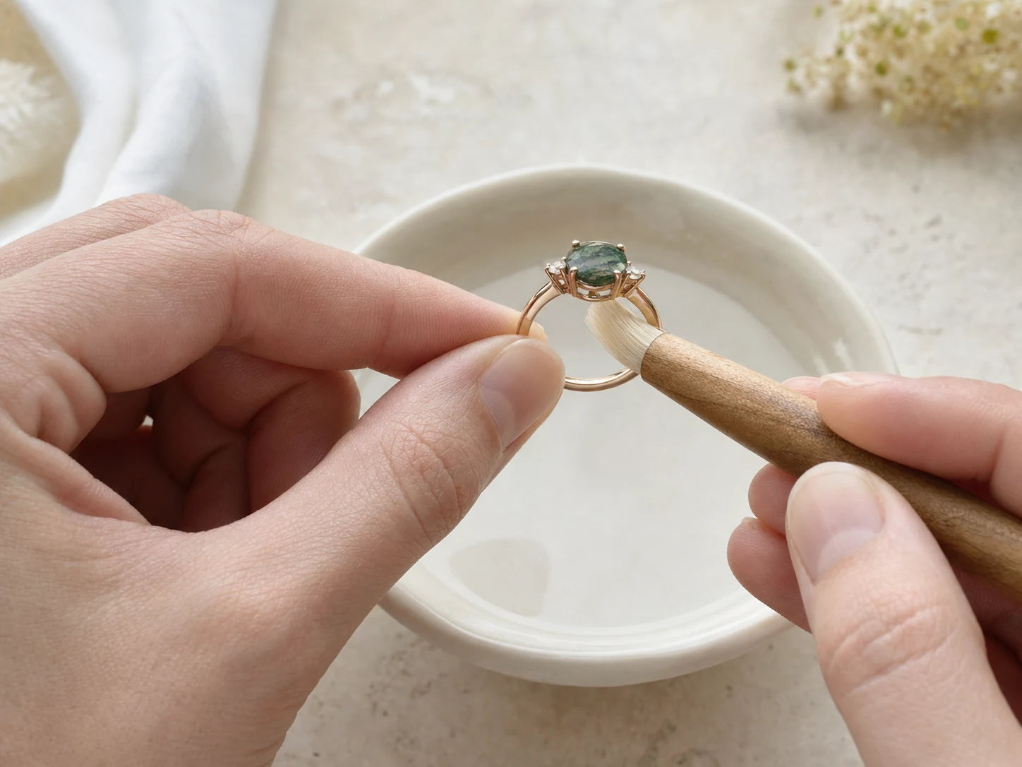A ring is gently cleaned with a soft brush above a bowl